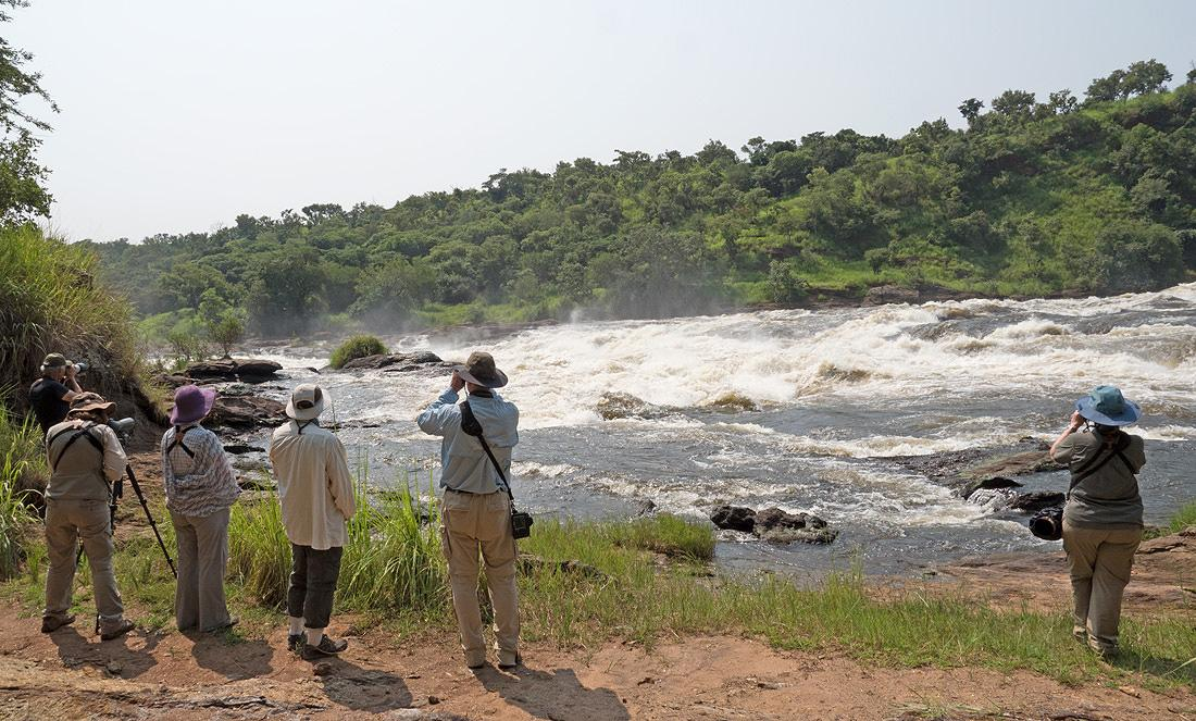 Visitors observing a river and waterfall in Uganda